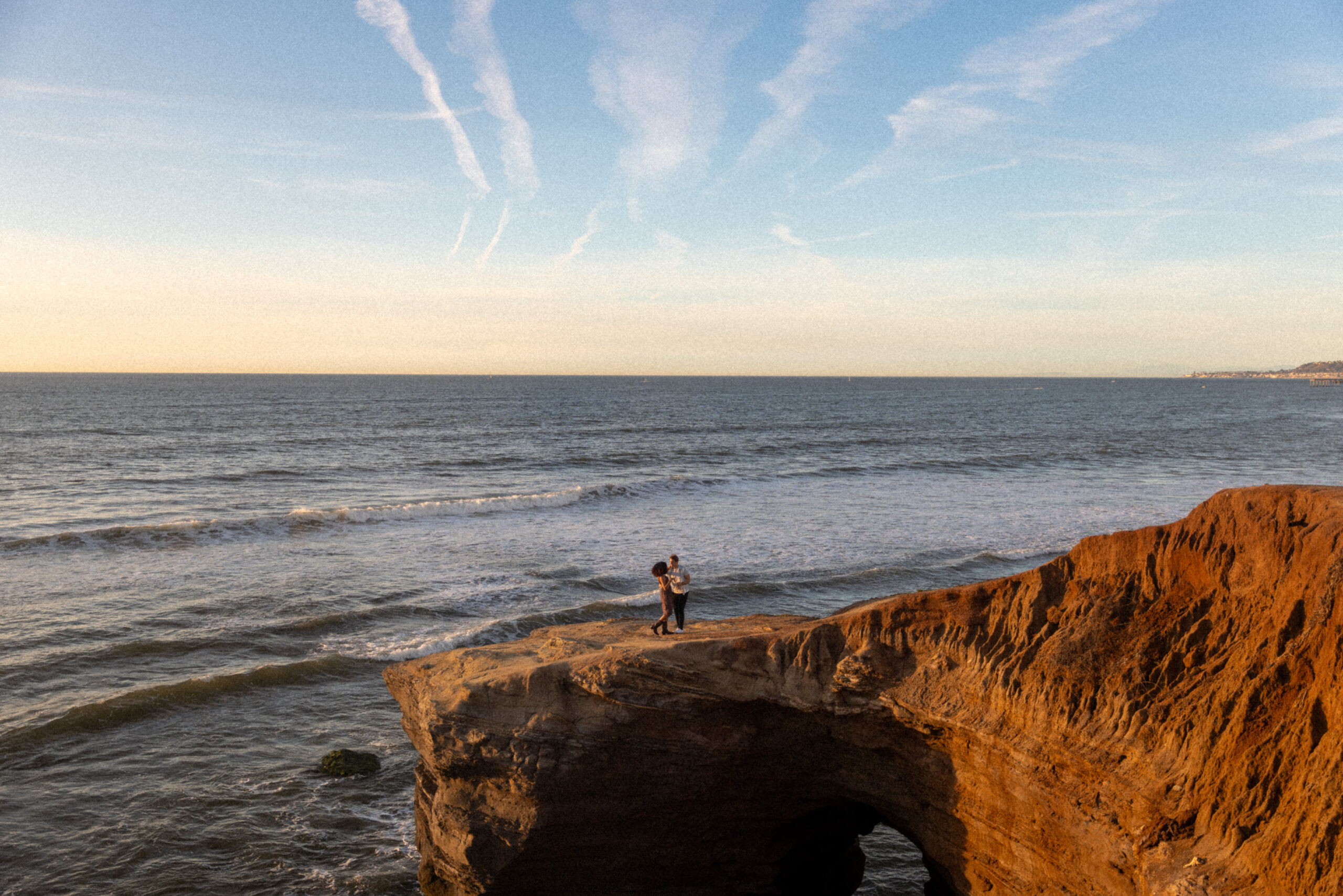 Couple dances on a rock with the ocean in background